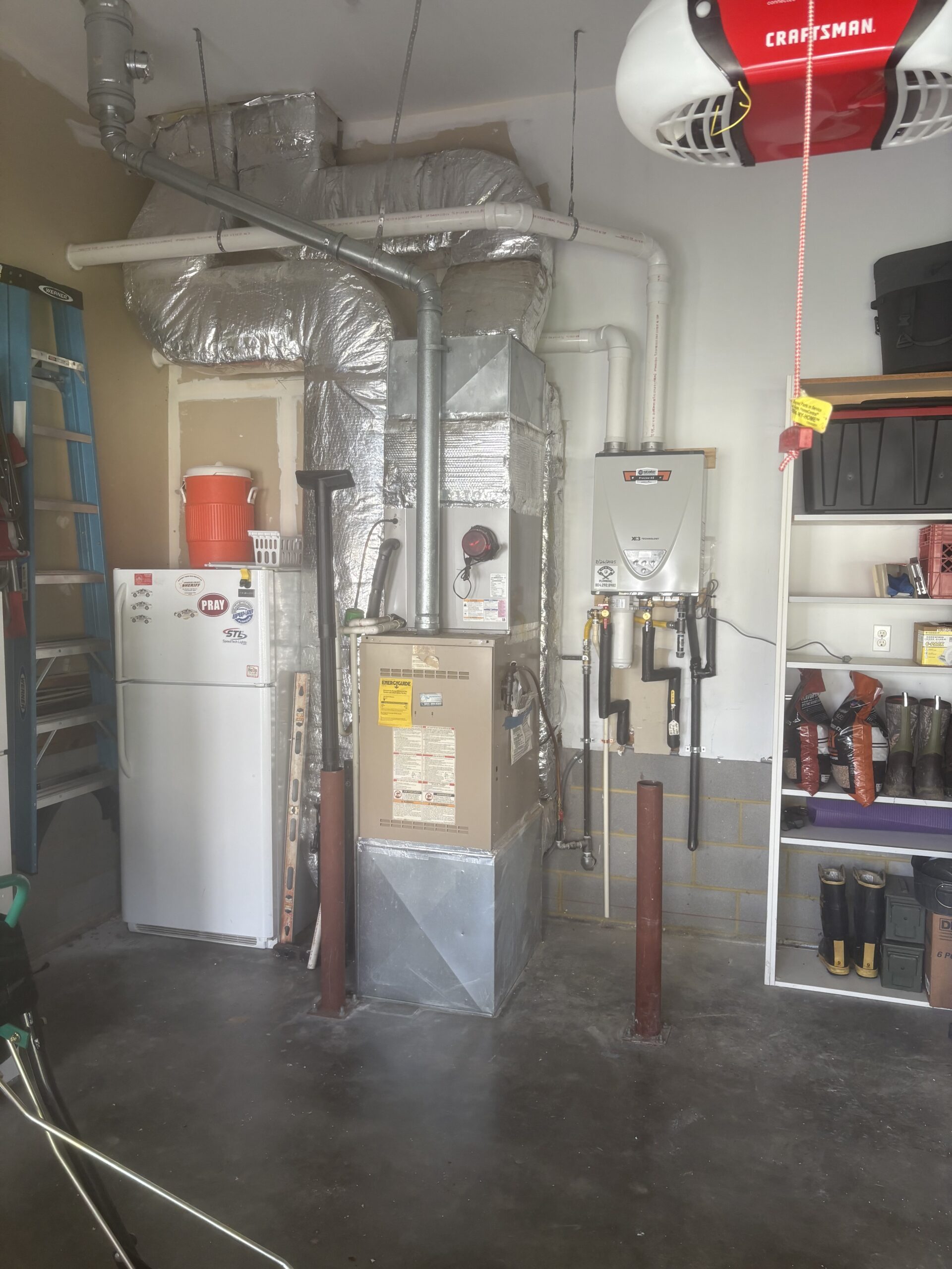 A garage utility area with an HVAC unit, water heater, refrigerator, washing machine, shelving, and various storage items along the walls.